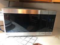 Full front view of the LG microwave showing stainless steel frame and black glass door on tiled surface.