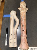 Photo of two ceramic flutes, one double-pipe with carved decorative top and another with single pipe and carved top, showing size relative to a marker pen.