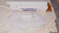 Partial roll of white Film Gard 6 mil plastic sheeting laid out with some loose folded sheets.