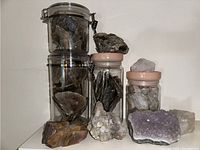 Overview of rocks and gems including amethyst cluster and quartz pieces, some stored in jars with lids.