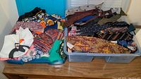 Wide view of plastic storage bin filled with scarves and ties, and additional folded scarves nearby.