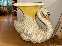 Side view of the swan shaped plant stand showing the detailed feathers and yellow top surface.