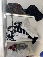 Top shelf and middle shelf show various folded towels and fabrics, including white textured towel, black fabric, multicolored patterned fabric, and black and white floral fabric.