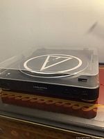 Black Audio-Technica turntable with a clear plastic dust cover and logo visible on the platter mat. Front panel with control buttons visible.