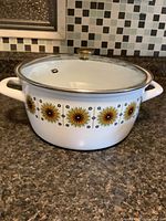 Front view of large white enamel stock pot with sunflower pattern and glass lid showing brass knob.