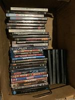 Box of assorted DVDs stacked with titles visible on some spines