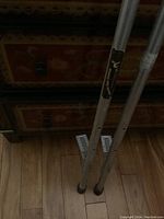 Full length photo showing two aluminum stilts with foot platforms resting on wooden floor in front of a decorative wooden piece of furniture.