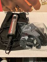 Philips hair trimmer with power adapter and multiple comb attachments in plastic bag placed on a black travel pouch.