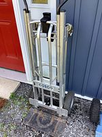 Front view of the Cosco hand cart showing the aluminum frame, handles, and loading platform with signs of wear and rust.