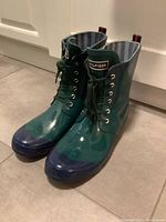 Pair of green and navy blue lace-up rain boots from front angle.