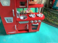 Front view of red wooden play kitchen including fridge, stove, sink, and oven