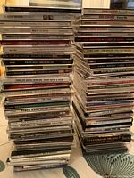 Photo showing multiple stacked CD cases with visible titles from various artists and genres, mostly country and pop music.