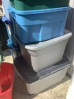 Stack of assorted plastic storage totes in blue, gray, and green with some containing lids and others missing lids.