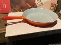Top view of the frying pan showing white/light gray enamel interior and orange handle.