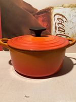 Front view of the flaming orange round cast iron pot with lid and black knob.