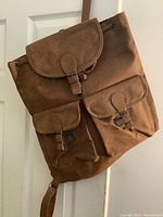 Brown leather backpack showing front view with flap and buckle closures on main and front pockets.