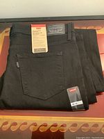 Black folded Levi's jeans with size label 32x32 visible, and leather patch on waistband.