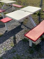Outdoor picnic table with white fiberglass top and red benches, metal legs, placed on gravel.