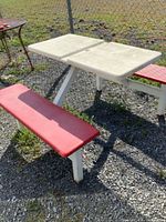 Fiberglass and metal picnic table with white top and red benches shown outdoors on gravel