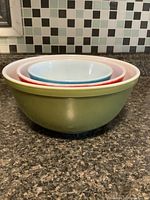 Three nested Pyrex mixing bowls on kitchen countertop against tiled backsplash.
