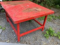 Red metal heavy-duty square table showing surface wear and dirt on top.