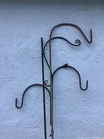 Two black metal shepherds hooks with curved ends and one with decorative curl hanging on a wall.