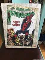 Photo of 11 x 14 canvas art board showing cover of The Amazing Spider-Man #68 titled 'Crisis on Campus' with Spider-Man and protesting students.