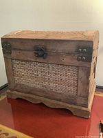 Front view of small wooden chest showing lidded top, metal latch, and woven thatched panels on front and sides.