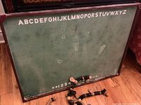 Photo of green chalkboard side showing alphabet and numbers with wooden counting disks arranged on floor