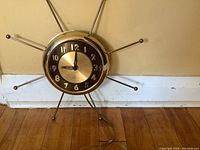Front view of vintage sunburst style wall clock showing circular dial with metallic numbers and sunburst rods.