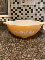 Side view of the large yellow vintage Pyrex mixing bowl showing white floral pattern and one pour spout