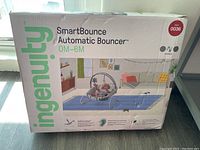 Photo of the Ingenuity SmartBounce Automatic Bouncer box showing product name, age range 0-6 months, and product image with baby inside bouncer.