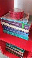 Stack of books including anatomy, physiology, pathophysiology, orthopedic physical assessment, slow cooker recipe book with a roll of red raffle tickets on top.