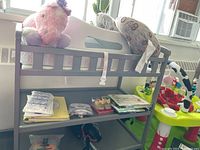 Gray wooden baby changing table holding children's books, various baby items, and stuffed animal placed on top