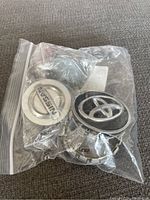 Four automotive centre caps including two Toyota and two Nissan in plastic bag on fabric surface.