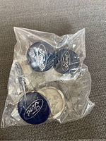Six Ford centre caps in a plastic bag on carpeted floor, showing logo and condition.