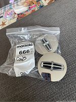 Three Lincoln center caps in a plastic bag showing front and back sides with Lincoln emblem.