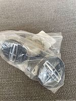 Plastic bag containing four black Lincoln center caps with silver emblem visible through the bag.