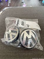 Two Volkswagen wheel centre caps visible inside a clear plastic zip bag, showing VW logo prominently, one larger than the other.