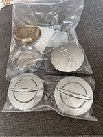 Three Jeep and two Chrysler center caps in plastic bags on fabric surface.