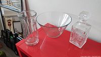 Wide view of glass bowl, vase, and cut glass decanter on a red surface