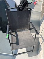 Photo of black metal framed outdoor folding chair with mesh seat and back, showing chair fully opened with armrests and metal frame.