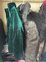 Side view of two hung jackets: a green velvet quilted jacket and camo jacket with fur hood.