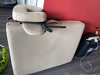 Full view of the folded beige massage table with attached padded U-shaped headrest, showing smooth upholstery and black support bars.