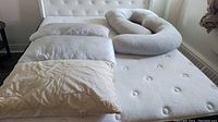 Four pillows on a mattress: two white standard pillows, one large beige pillow, one gray body pillow shaped for support.