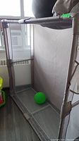 Front angled photo of taupe colored fabric and mesh play pen with green ball inside.