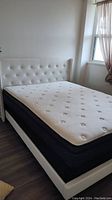 Full view of the bed with tufted white faux leather headboard and mattress.