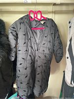 Black infant snowsuit hanging on pink hanger showing dinosaur pattern and zipper.