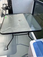 Photo of an outdoor square table with metal frame and plexiglass top, showing some rust and wear.