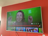 Photo of the front view of the LG TV turned on, playing children's educational video, showing the full TV mounted on the orange wall.